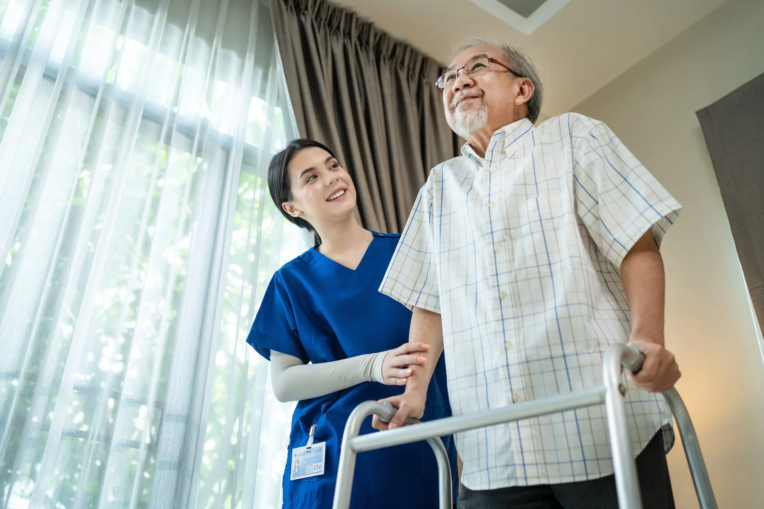 Asian Senior elderly disabled man patient walking slowly with walker at nursing home care. Caregiver therapist nurse support older handicapped male use Zimmer frame. Medical therapy insurance concept.